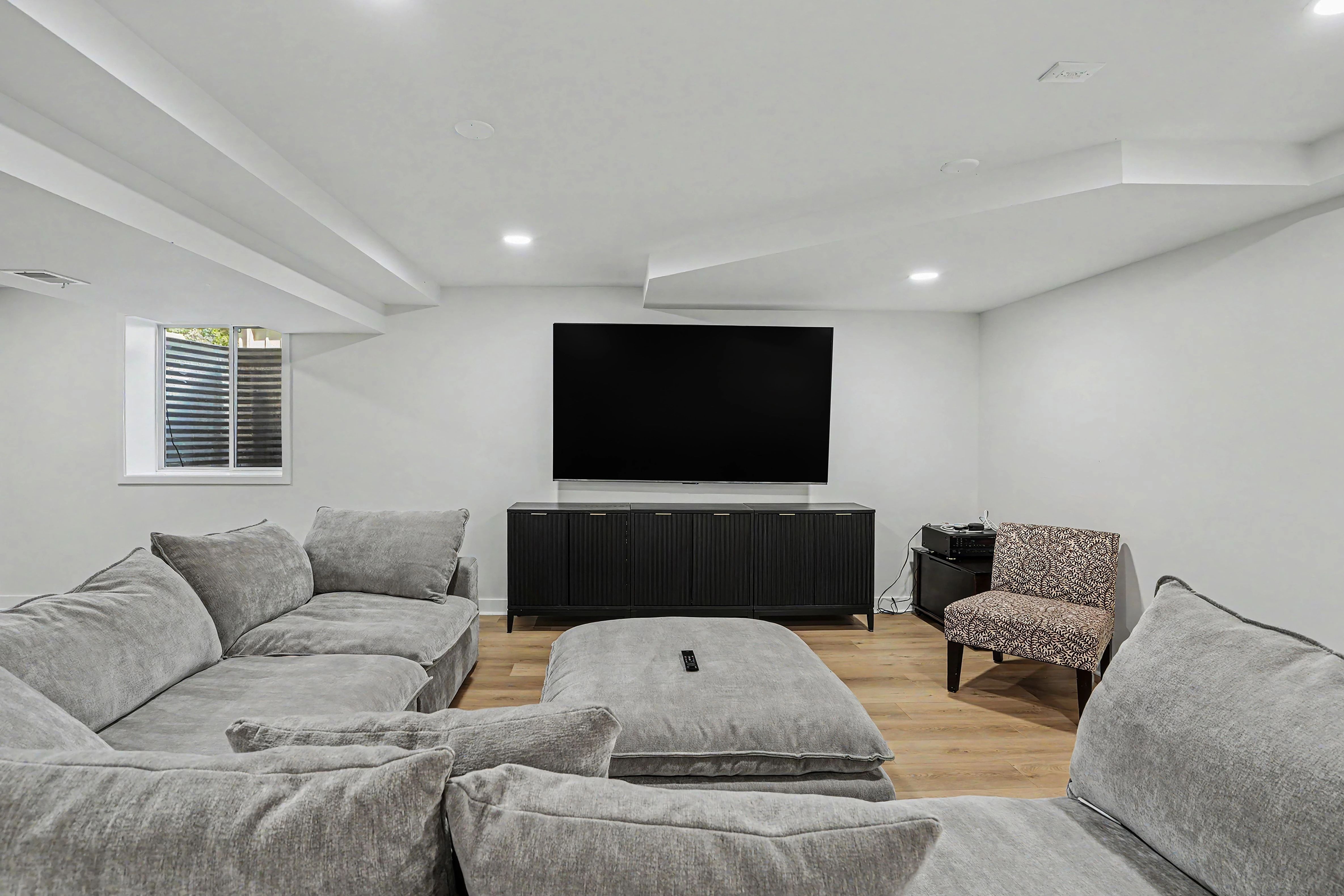 Finished basement family room with wall-mounted TV over a black media console and sectional seating