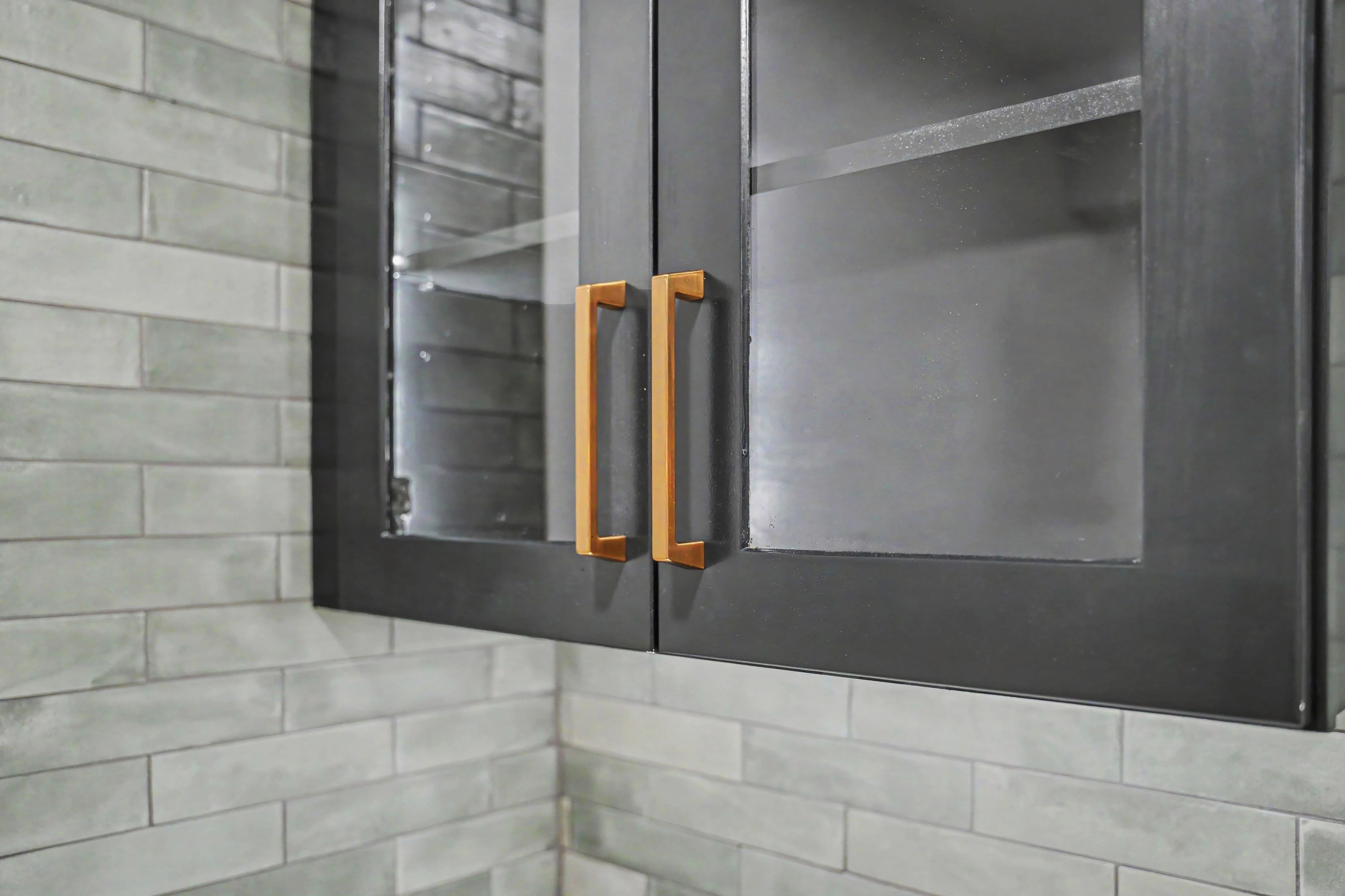 Glass front display cabinets with brass pulls over full height tile in a Prairie Village basement remodel