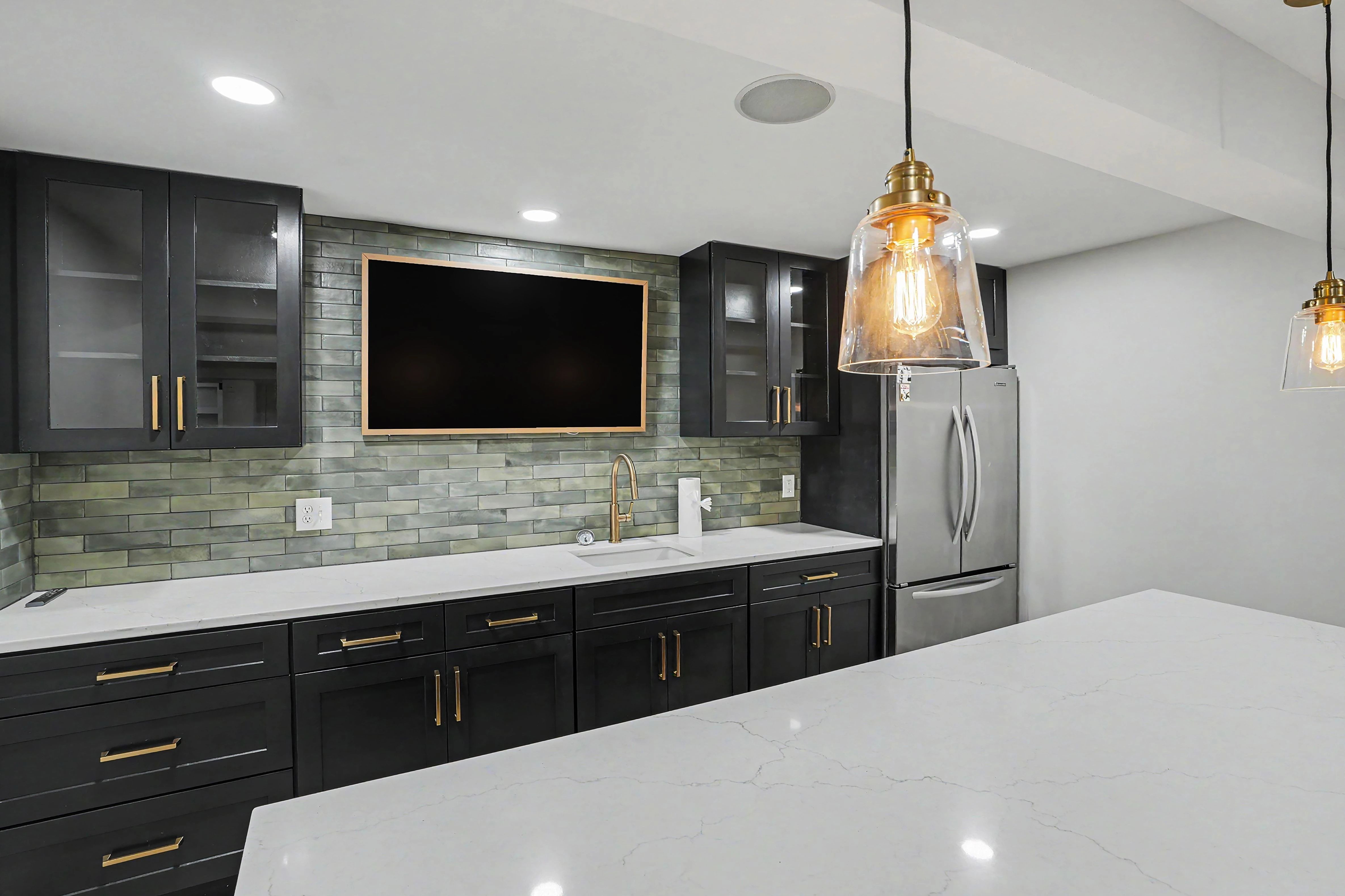 Kitchenette sink wall with full height tile backsplash and gold faucet in a Prairie Village basement remodel