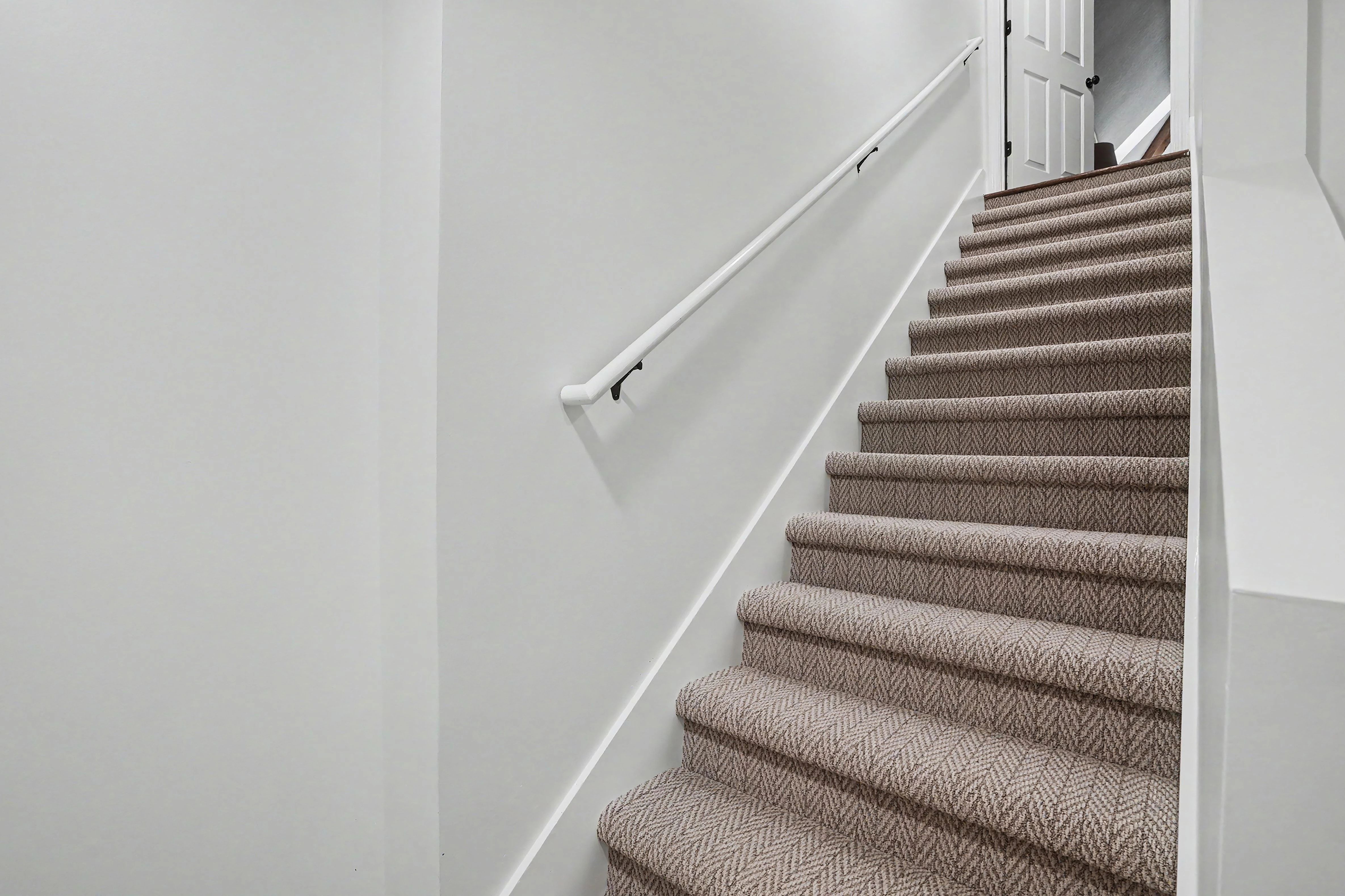 Finished basement stairwell with carpeted stairs and white handrail in a Prairie Village basement remodel