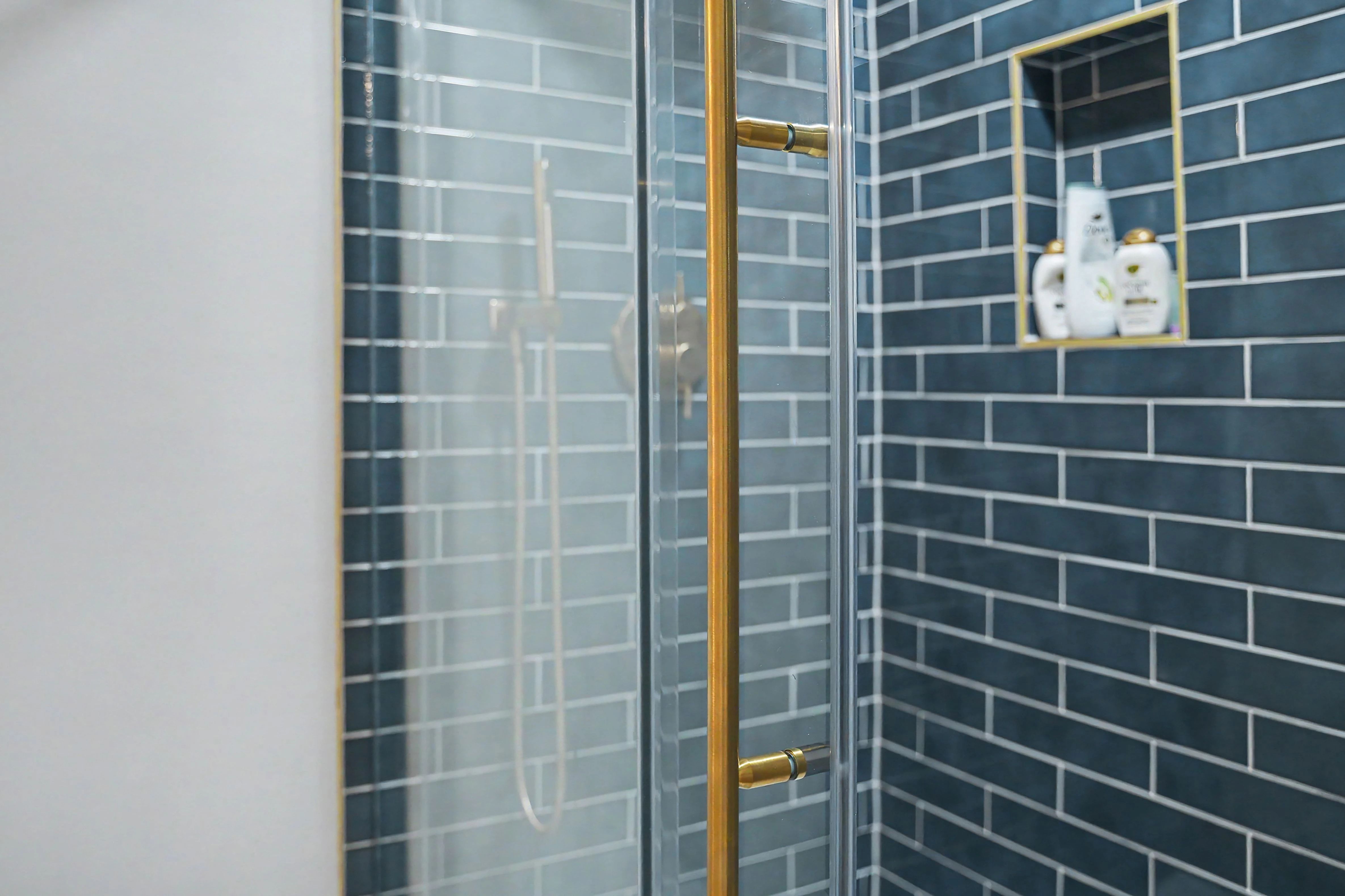 Tiled shower with brass glass door hardware and gold trimmed niche in a Prairie Village basement remodel